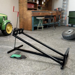 Schwarzer Juskys Rasentraktorheber mit Kurbel und Handschuhen im Werkstatt-Ambiente.