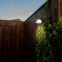 Lutec Solar-LED-Wandleuchte Moon, anthrazitfarben, an Holzwand mit Pflanzen.
