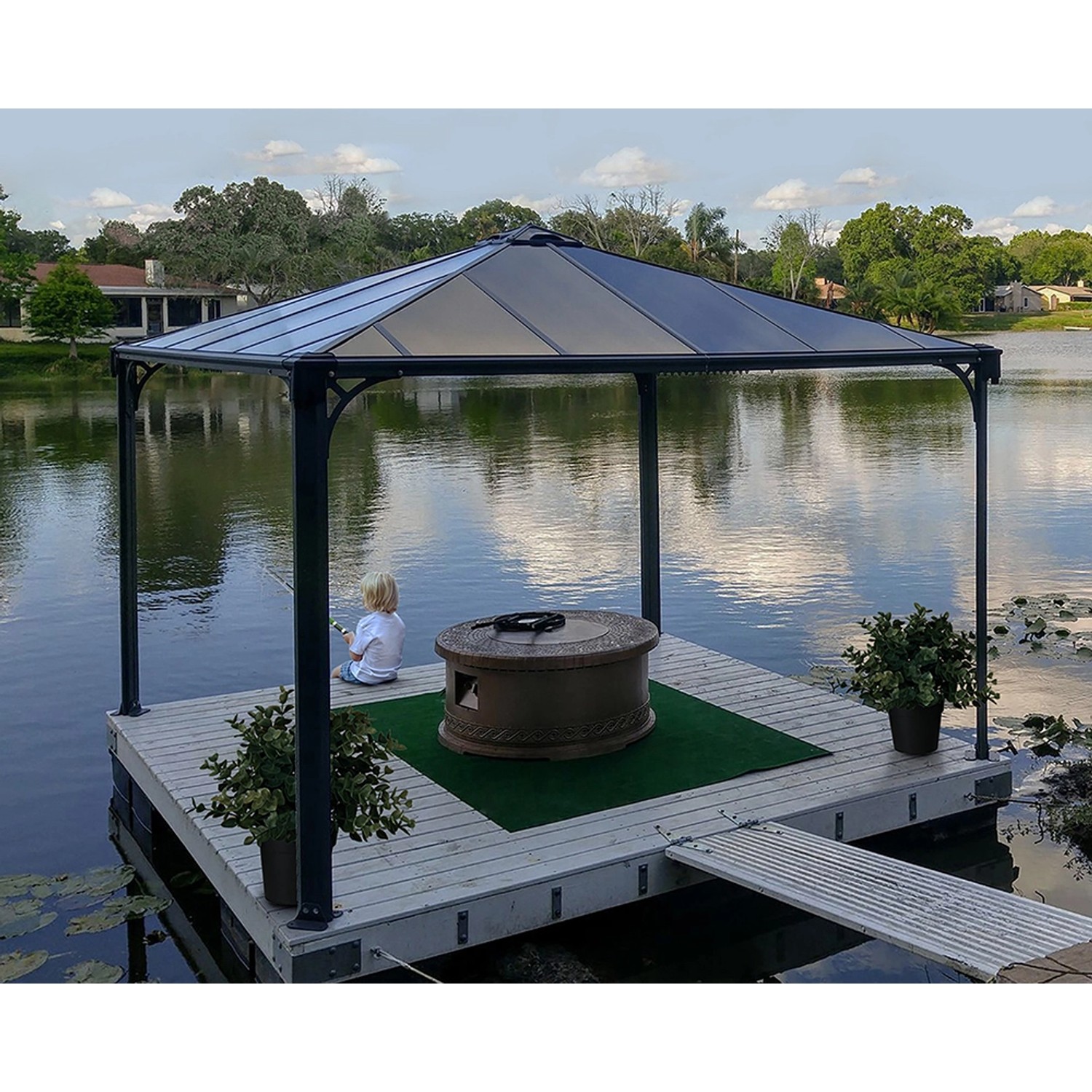 Anthrazitfarbener Palram Canopia Palermo Gartenpavillon 3.6x3.6 m mit LED-Set auf einem Steg am See.