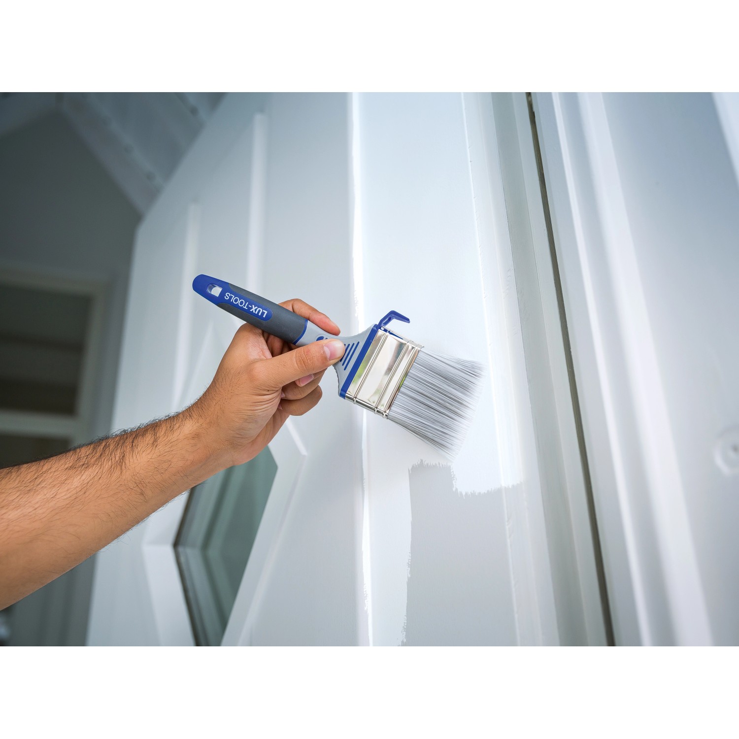 Hand streicht mit LUX Flachpinsel Lack 60mm eine weiße Tür. Pinsel mit Eimerhaken.