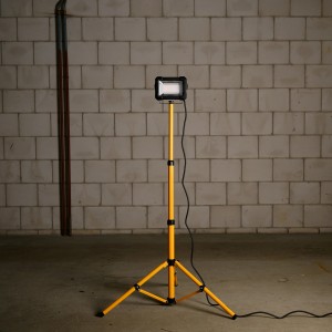 LED-Arbeitsleuchte 50W auf gelbem Stativ (163cm) vor Mauerwerk. Baustrahler für Innen & Außen.