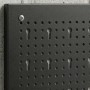 Schwarze, strukturierte Stahl-Lochwand mit runden Löchern und Schlüsselschlitzen, an Betonwand montiert. Für Werkstatt.