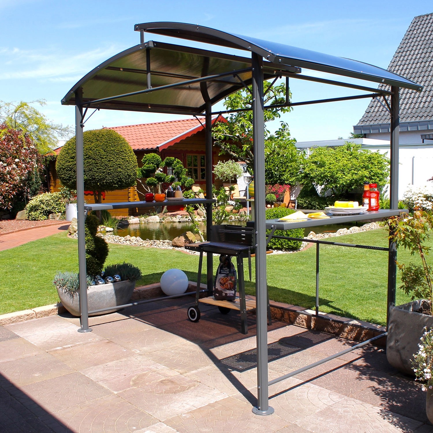 Leco Grillpavillon mit Polycarbonat-Dach in Anthrazit mit Ablagetischen und Grill im Garten.