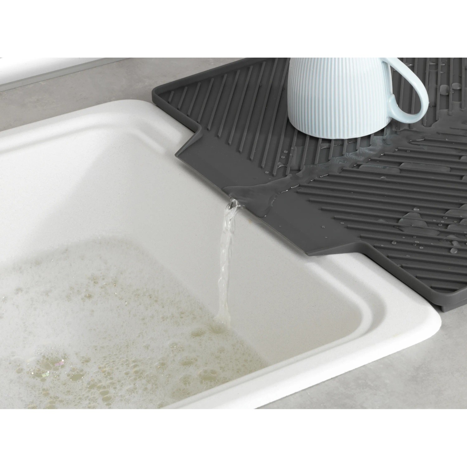 Graue Wenko Abtropfmatte Nelia Maxi aus Kunststoff mit Tasse auf einer Spüle, Wasser läuft ab.