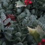 Nahaufnahme eines künstlichen Weihnachtskranzes mit grünen Blättern, roten Beeren und einem Zapfen. Detailreiche Deko.