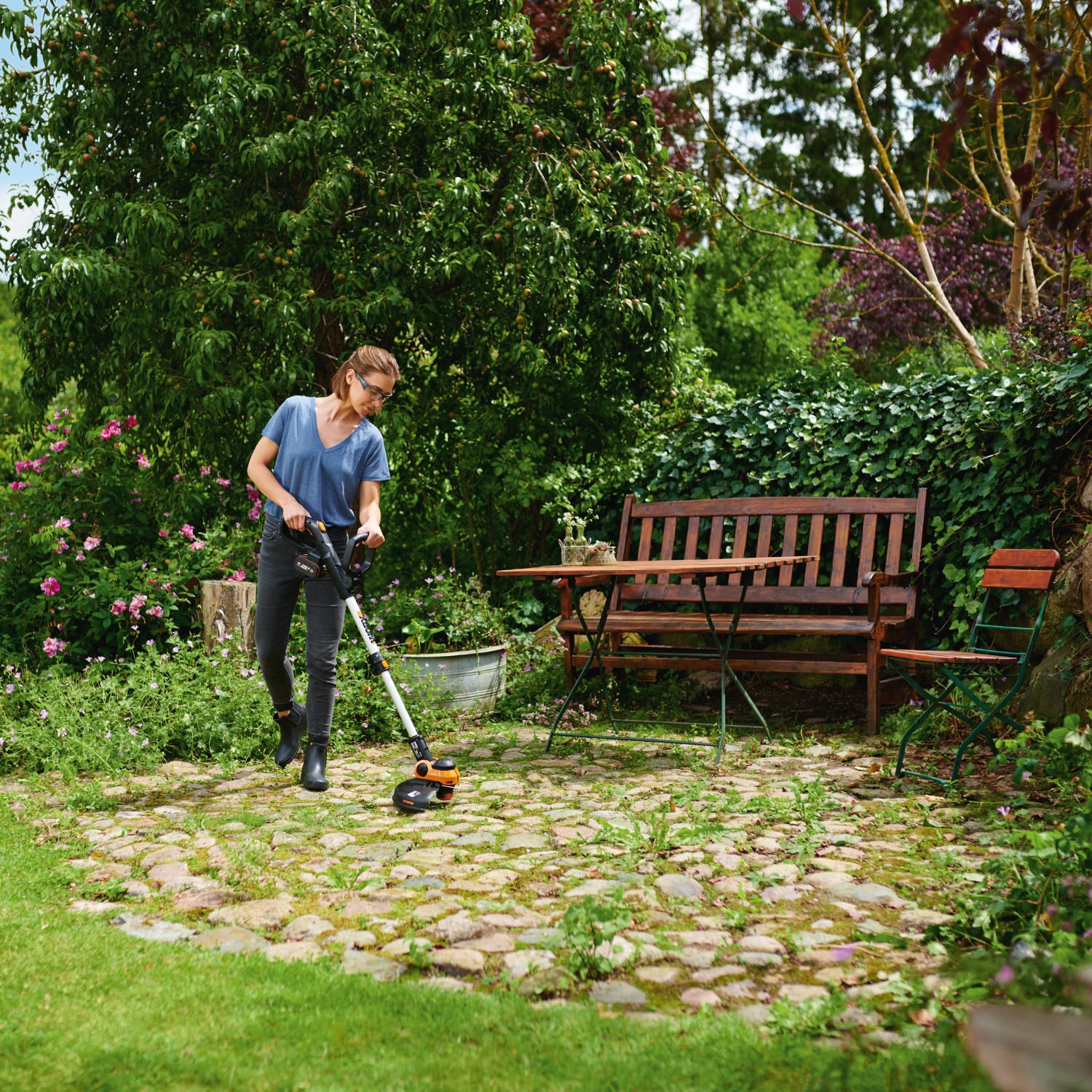 Frau trimmt Rasen mit Worx Akku-Rasentrimmer WG163E.9 im Garten.