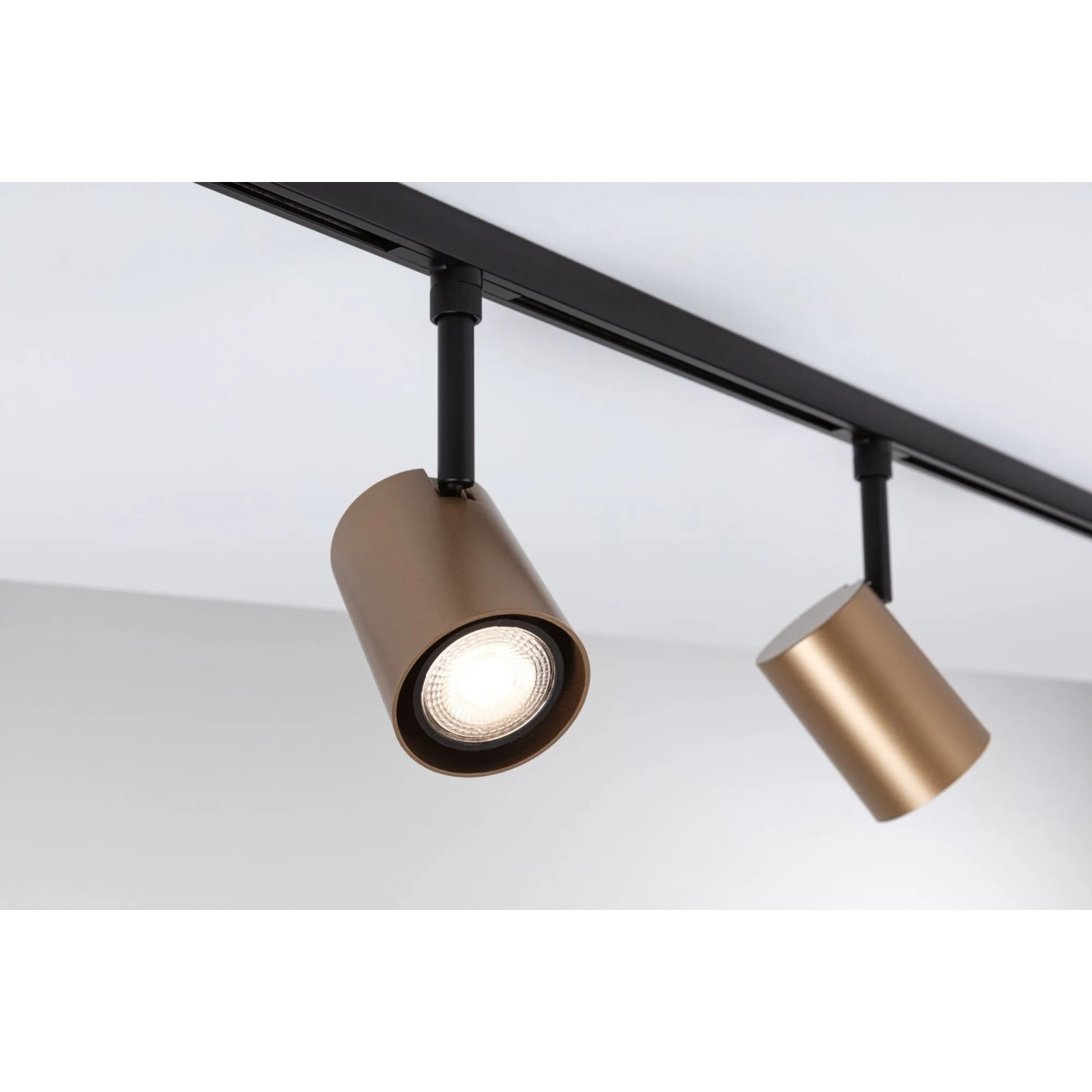 Zwei Paulmann URail Schienenspots Luxe in Gold matt und Schwarz an der Decke. Ein LED-Spot leuchtet hell.