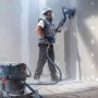 Anwender schleift Wand mit Exzenterschleifer und Staubabsaugung. Bosch Expert Schleifblatt für Zubehör.