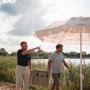 Zwei Personen tragen eine sandfarbene Petromax Kühlbox 25l am See.