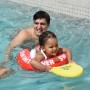 Kind mit rotem Freds Swim Academy Schwimmreifen Classic im Pool, begleitet von einem Erwachsenen.