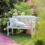 Weiße 2-Sitzer Gartenbank Glendale aus FSC®-Holz mit Kissen im Garten.