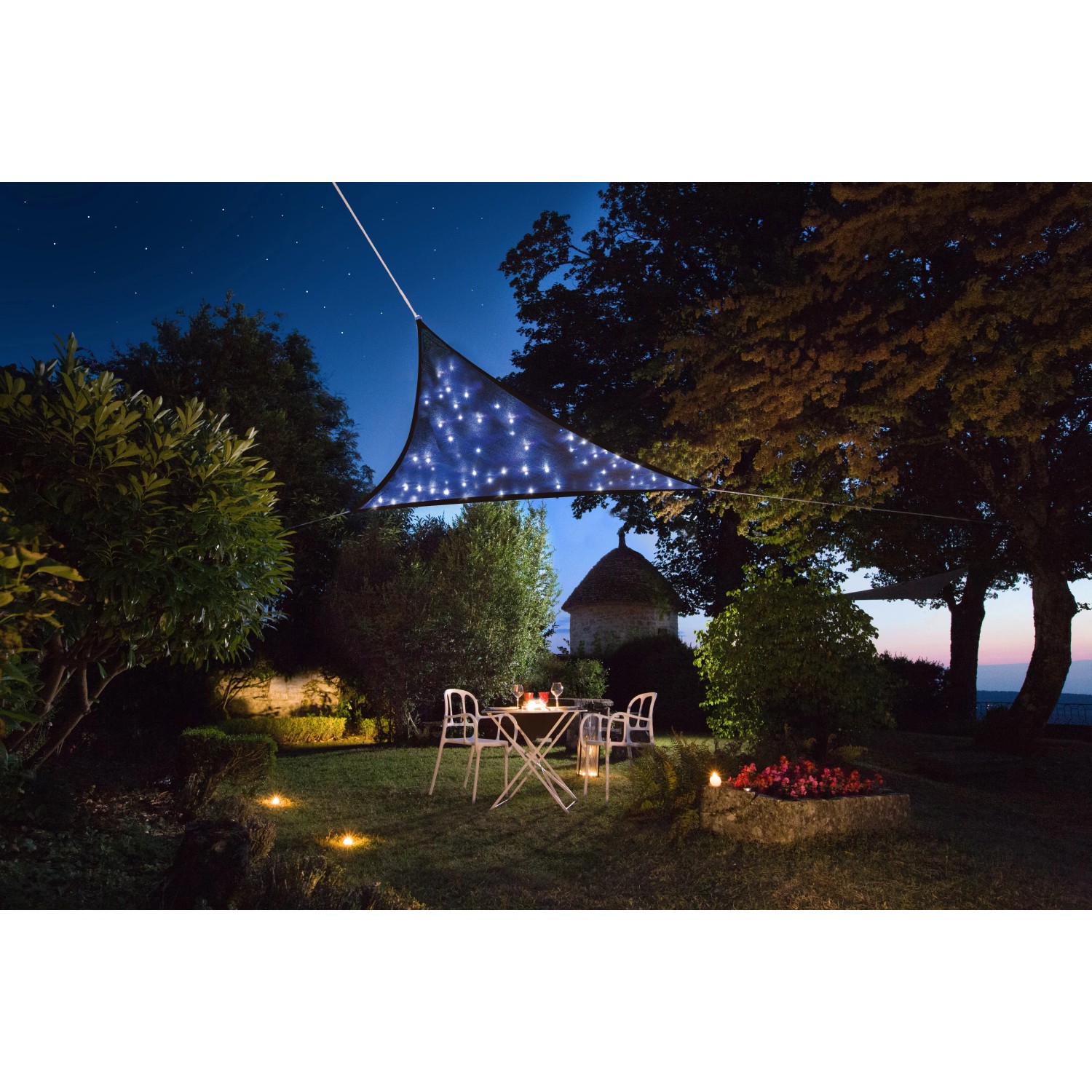 Dunkelblaues, dreieckiges Perel Sonnensegel mit LED-Beleuchtung über einer Gartensitzgruppe.