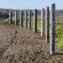 Reihe Gabiona Gabionen-Säulen, eckig, feuerverzinkt, gefüllt mit Steinen in verschiedenen Farben.