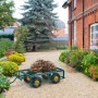 Dunkelgrüner Stahl Bollerwagen mit klappbaren Seiten, beladen mit Gartenabfällen, auf Kiesweg im Garten. Ideal für Transport.