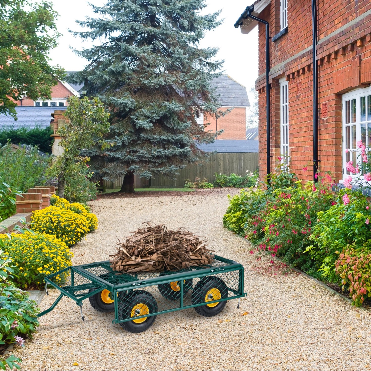 Dunkelgrüner Stahl Bollerwagen mit klappbaren Seiten, beladen mit Gartenabfällen, auf Kiesweg im Garten. Ideal für Transport.