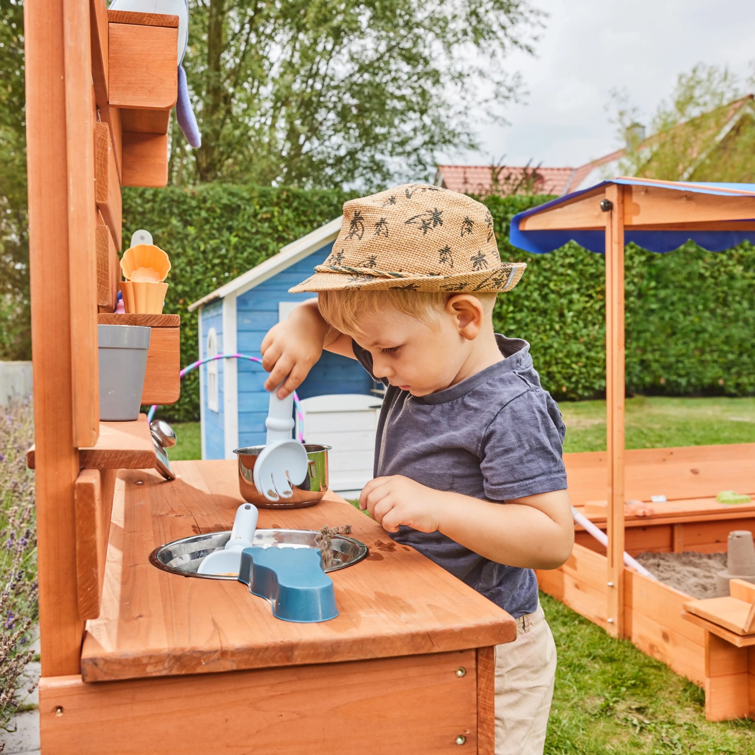 Kind spielt an Home Deluxe Spielküche Mandu aus Holz mit Zubehör im Garten.