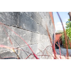 Dunkelgraue Mauersteine Collo Basalt mit gebrochenen Kanten, gestapelt als Gartenmauer. Rotes Ziergras im Vordergrund.