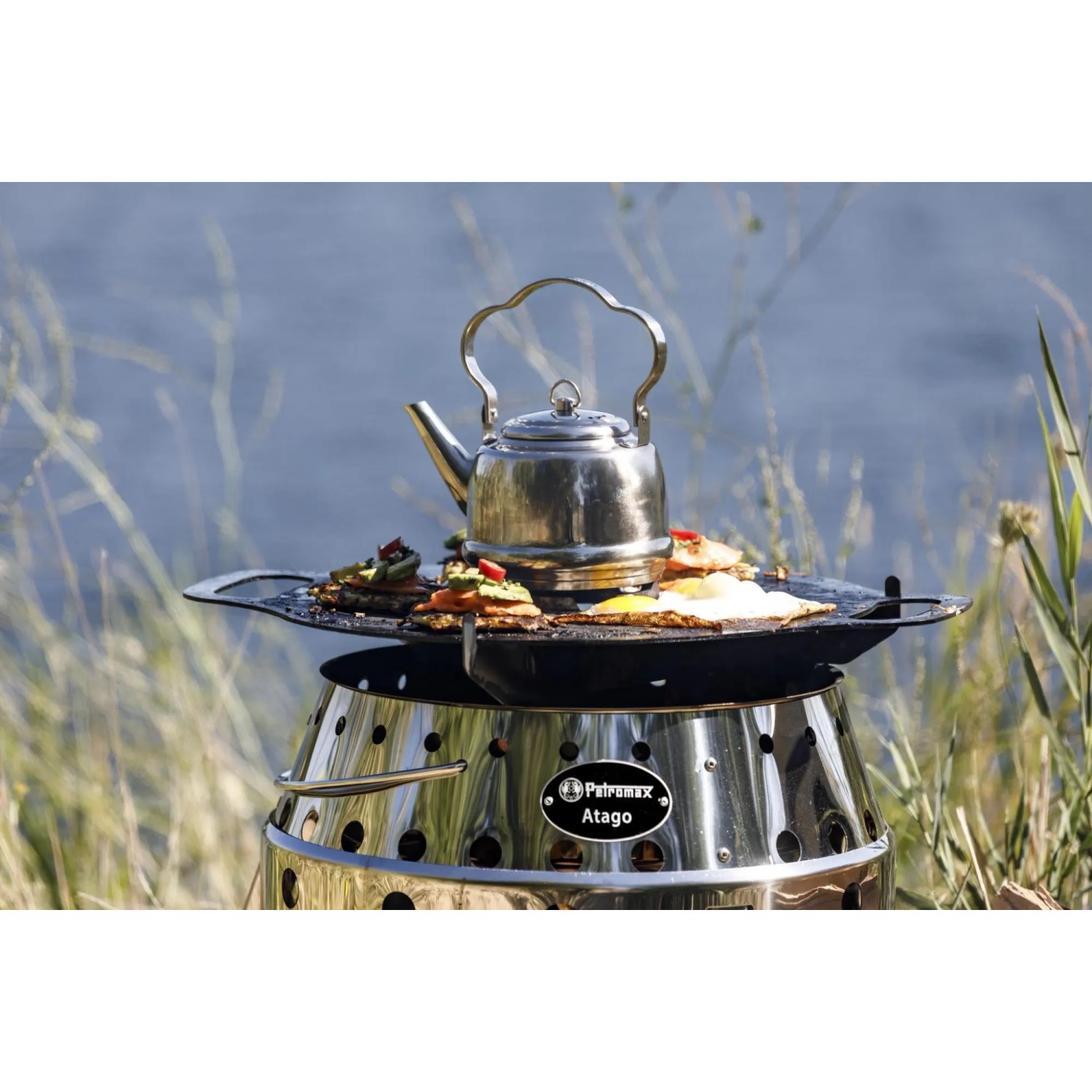 Petromax Grillplatte für Atago mit Speisen und Teekessel auf dem Grill.