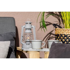 Feuerhand Sturmlaterne Baby Special Grau auf Tisch mit Tassen und Pflanze.