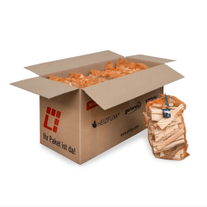 Offener Karton mit mehreren orangefarbenen Netzsäcken Heizfuxx Anzündholz aus Nadelholz. Ein Sack steht daneben. Ideal für Kamin & Feuerschalen.