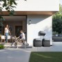 Anker Solix Solarbank mit Power Dock und Solarmodulen am Haus, Paar mit Hund im Vordergrund.
