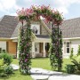 Schwarzer Costway Rosenbogen aus Metall, bewachsen mit rosa Blüten, als Gartendeko.