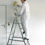 Mann streicht Wand stehend auf Krause Stufen Stehleiter Corda mit 6 Stufen.