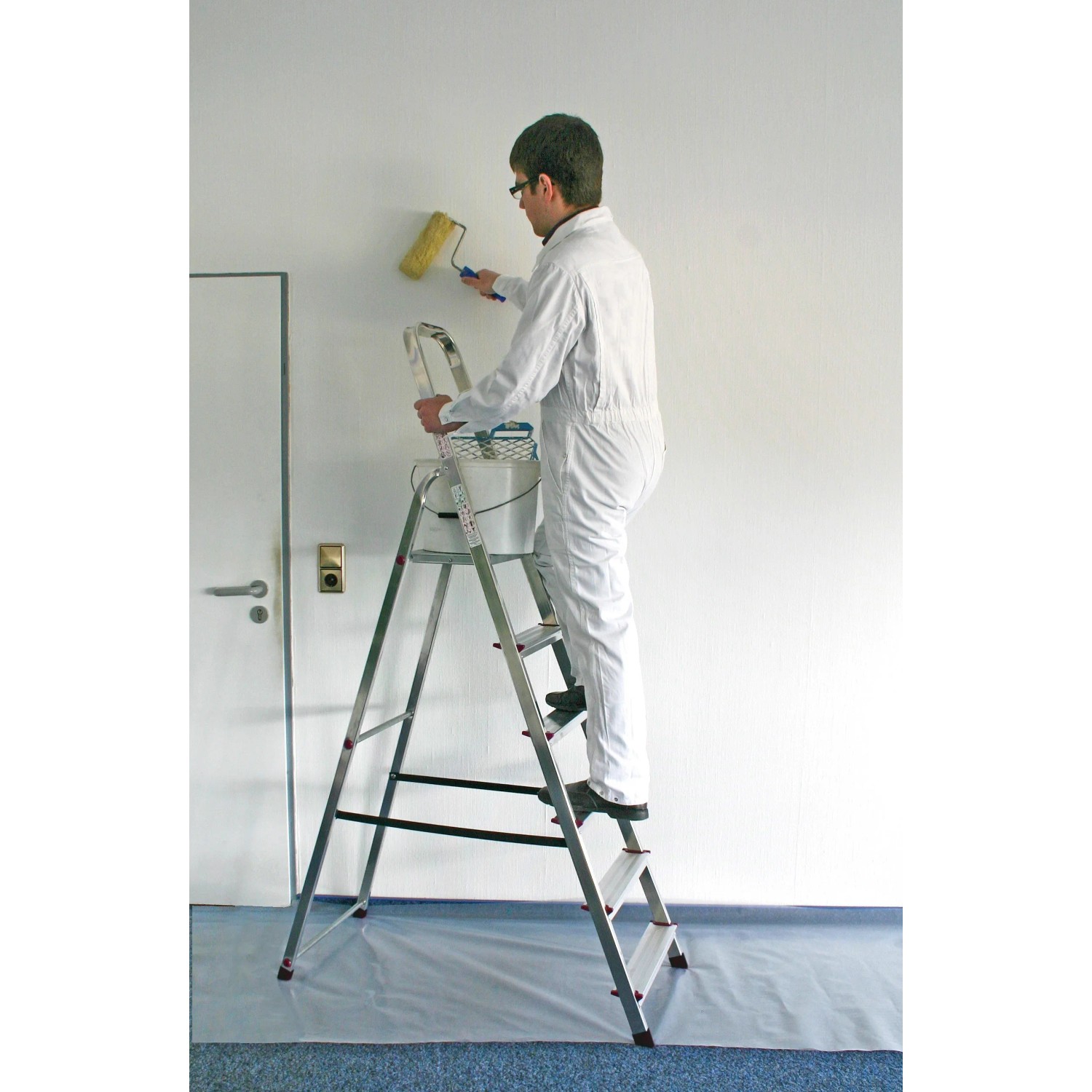 Mann streicht Wand stehend auf Krause Stufen Stehleiter Corda mit 6 Stufen.