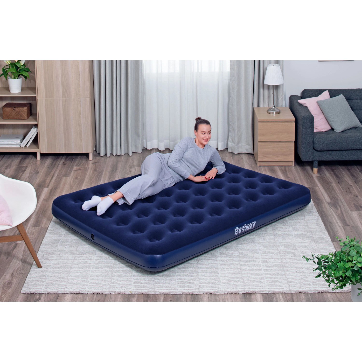 Bestway Luftmatratze Queen Size, dunkelblau, 203x152x22 cm, mit liegender Person im Wohnraum.