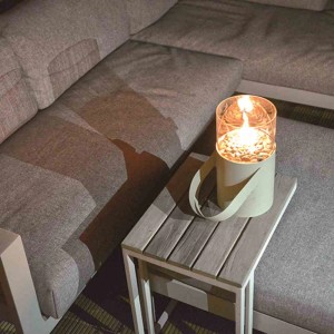 Weiße Cosi Gaslaterne Cosiscoop auf Tisch neben grauer Couch. Terrassenheizstrahler mit Glasaufsatz und Tragegriff.