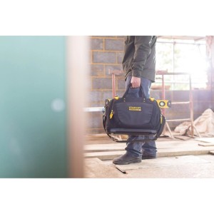 Person trägt schwarze Stanley FatMax Quick Access Werkzeugtasche mit gelben Akzenten auf Baustelle.