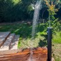 Schwarze Gre Solardusche aus Aluminium (18 l) im Garten mit laufendem Wasser.