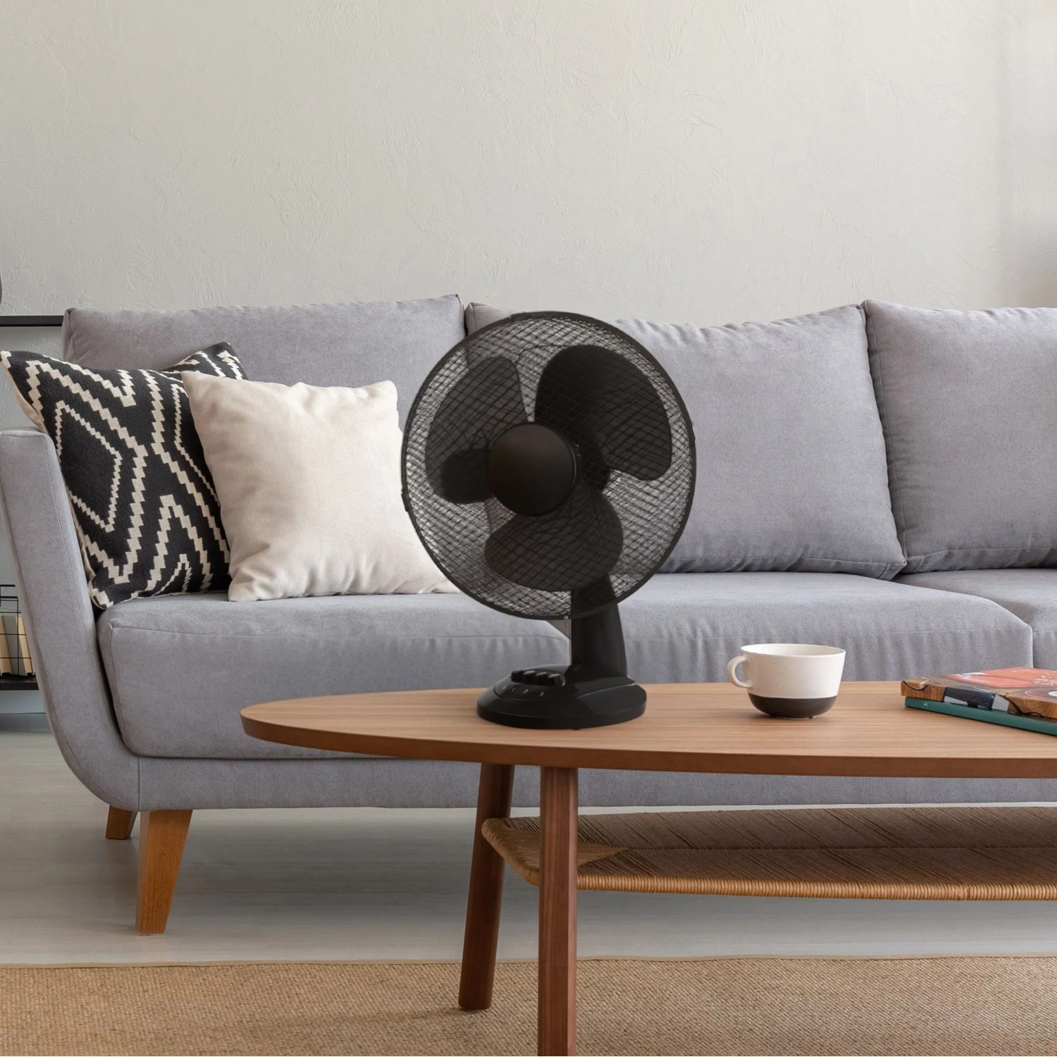 Schwarzer CMI Tischventilator (Ø 30 cm) auf Wohnzimmertisch vor grauem Sofa.