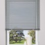 Silberne Aluminium Jalousie Burgos, 120x160 cm, am Fenster mit Blick ins Grüne.