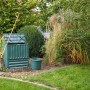 Grüner Garantia Komposter Comfort Eco-King 600 l im Garten mit Laubrechen und Eimer.