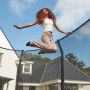 Frau springt auf grünem Salta Trampolin First Class ø 366 cm mit Sicherheitsnetz im Garten.