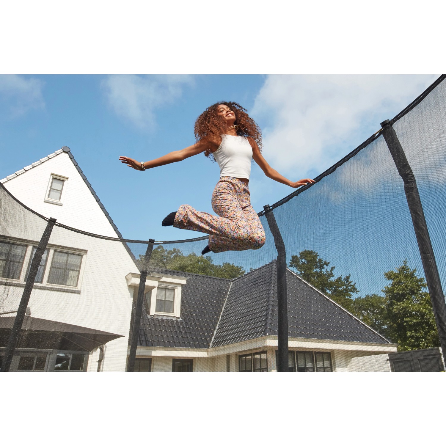 Frau springt auf grünem Salta Trampolin First Class ø 366 cm mit Sicherheitsnetz im Garten.
