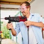 Einhell Bohrhammer TE-RH 950 5F in Aktion: Mann bohrt mit rotem Bohrhammer in Wand. Inkl. Koffer und Tiefenanschlag.