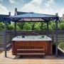 Palram Palermo 3x3 Gartenpavillon Anthrazit mit LED über Whirlpool und Sitzbank im Garten.