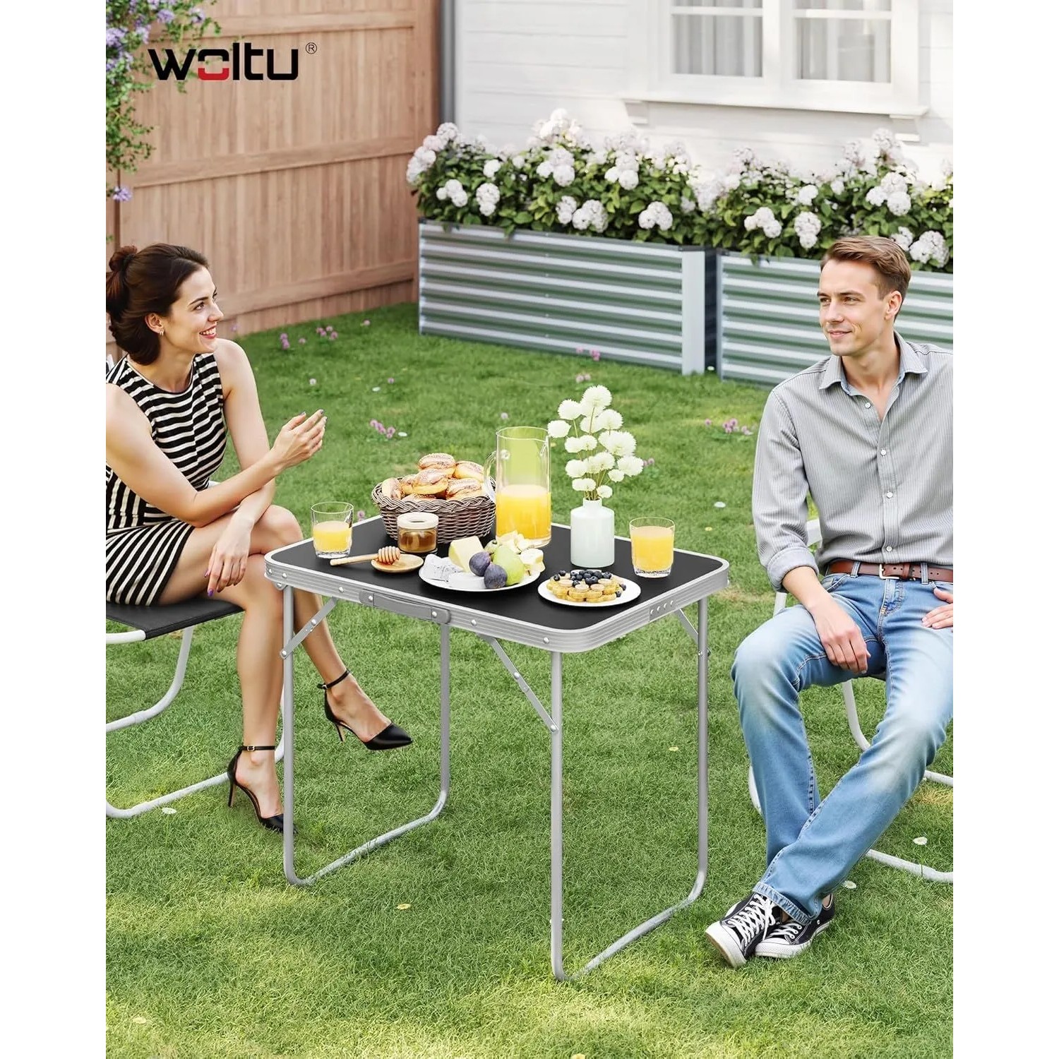 Schwarzer WOLTU Campingtisch Klapptisch aus Alu, mit zwei Personen im Garten.