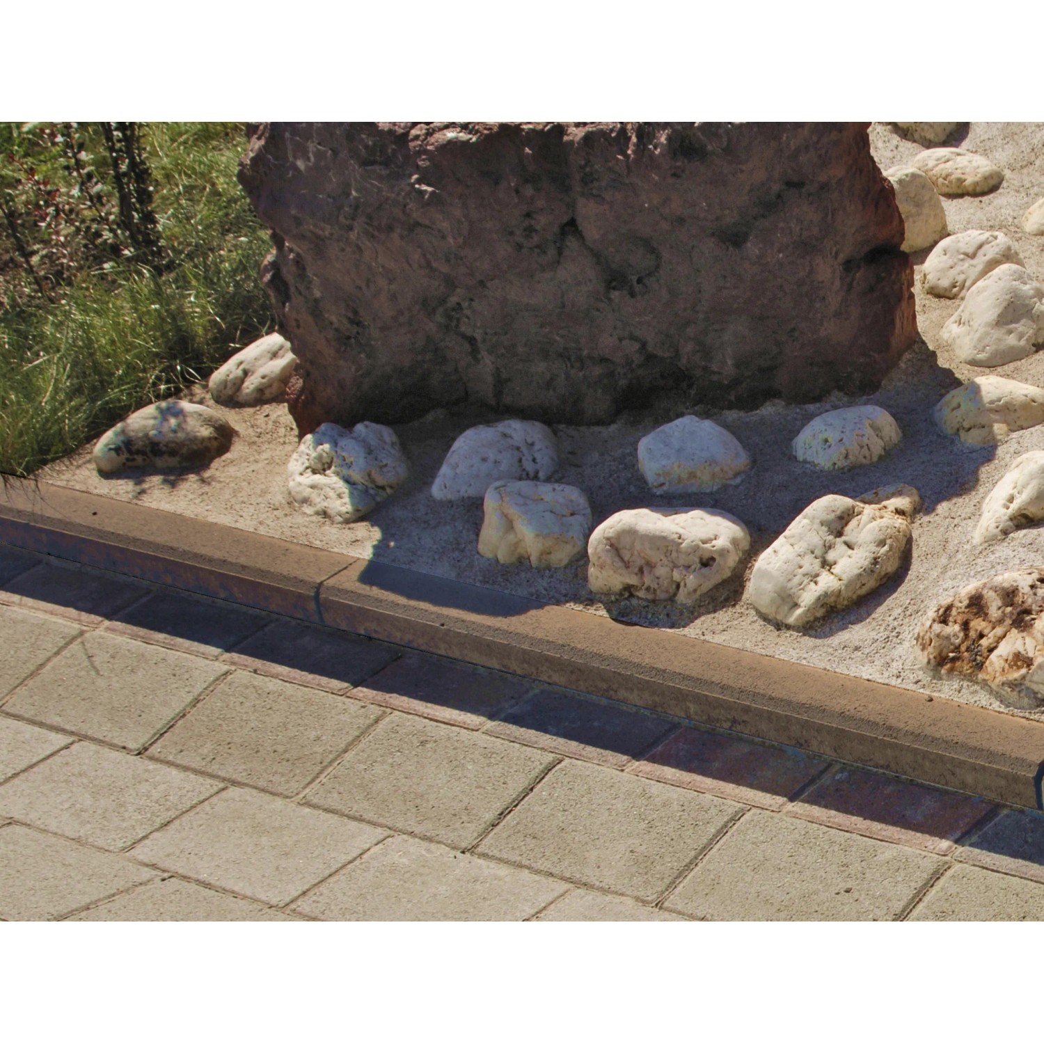 Brauner Tiefbordstein aus Beton (8x30x100 cm) als Beeteinfassung im Garten.