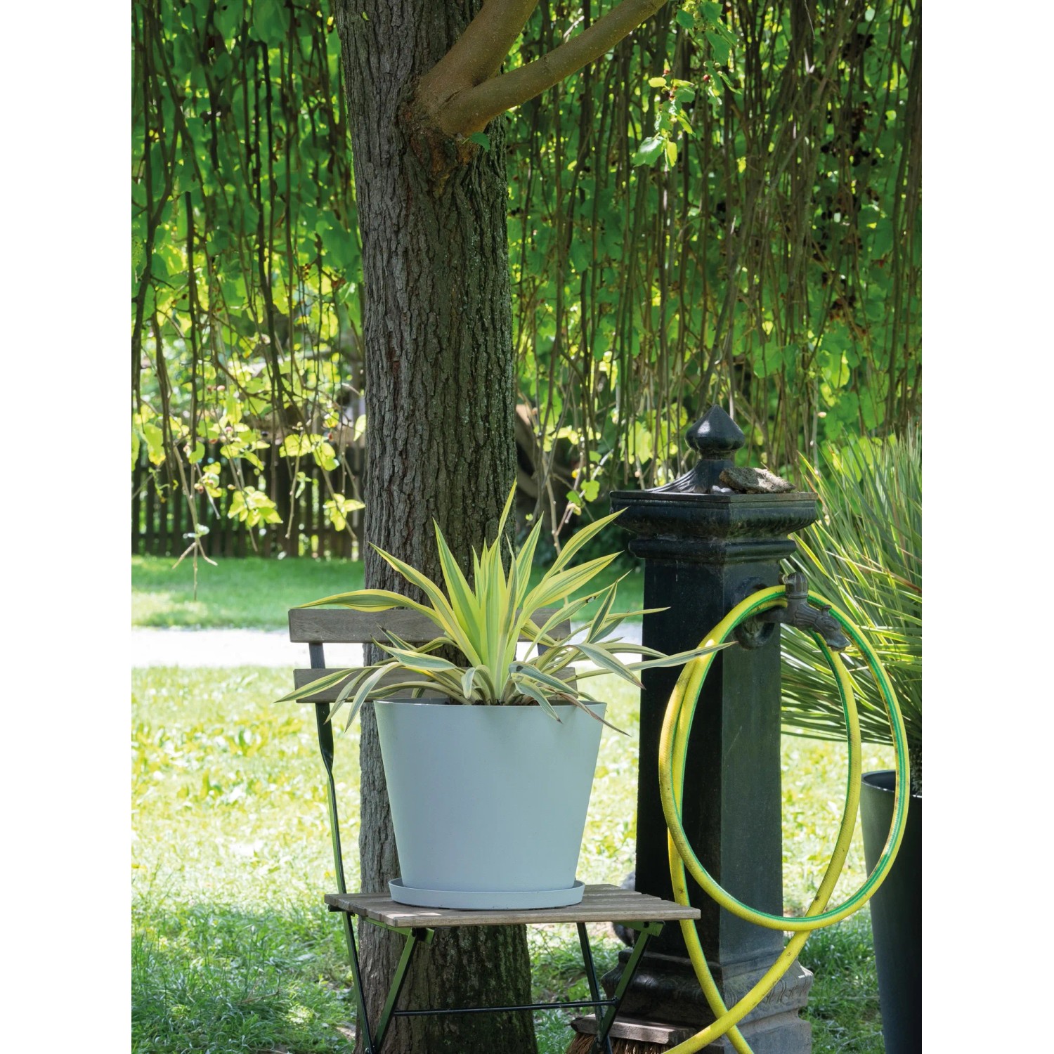 Heller, runder Deroma Untersetzer Origin Saucer 32 cm unter einem Topf mit Pflanze im Garten.