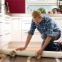 Mann verlegt Bodenbelag mit Tesa doppelseitigem Klebeband Eco Fixation. Klebeband und Bodenbelag im Fokus.