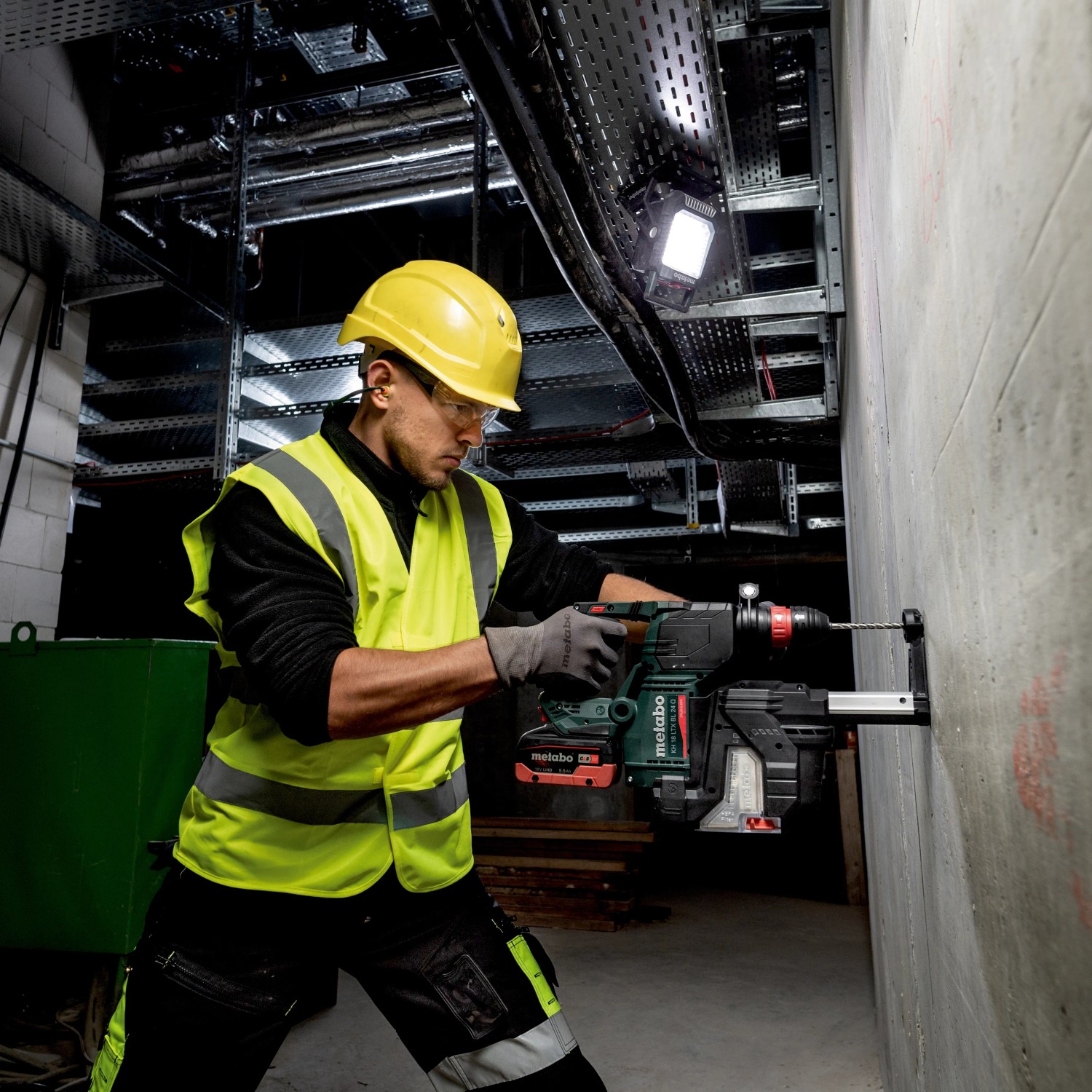 Mann bohrt mit Metabo Akku-Bohrhammer unter dem Licht des Metabo Akku-Baustrahlers BSA 18 LED 4000.