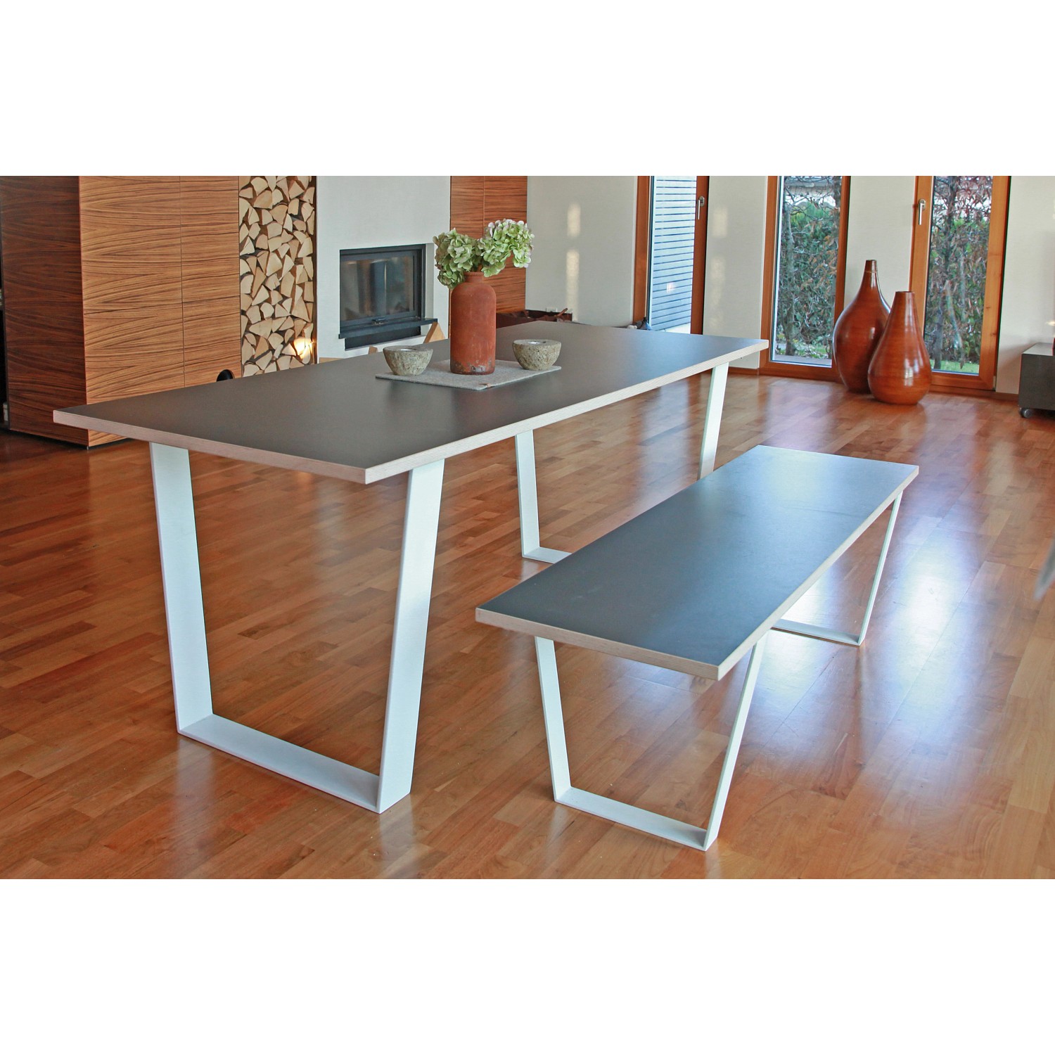 Tisch mit weißem Tischuntergestell in V-Form und passender Bank im Wohnraum.