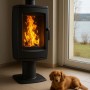 Schwarzer Plamen Gusskaminofen Aria (8 kW) mit Feuer im Brennraum und davor liegendem Dackel.
