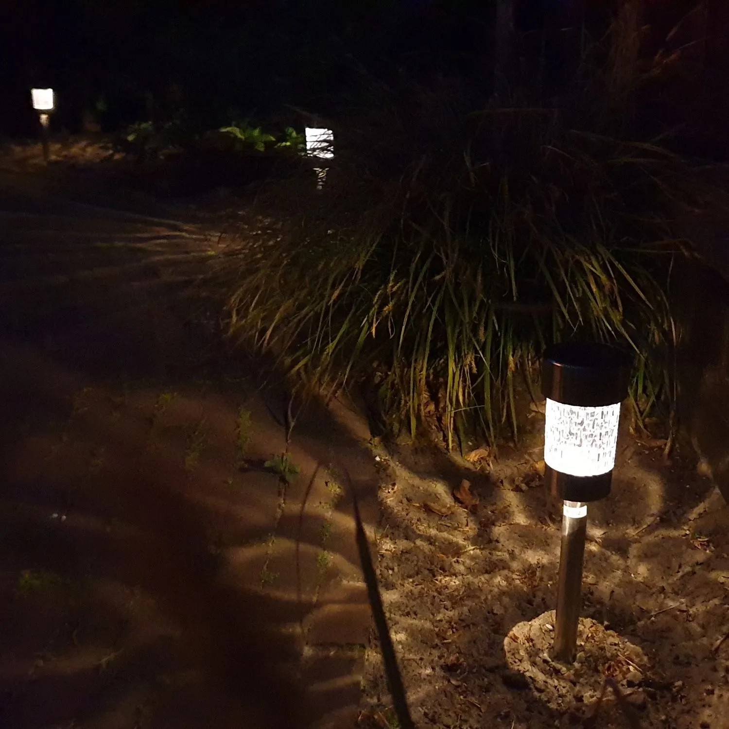 Zehn beleuchtete LED Solar Wegleuchten aus Edelstahl mit Erdspieß im Garten bei Nacht, erzeugen warmweißes Licht und Muster.