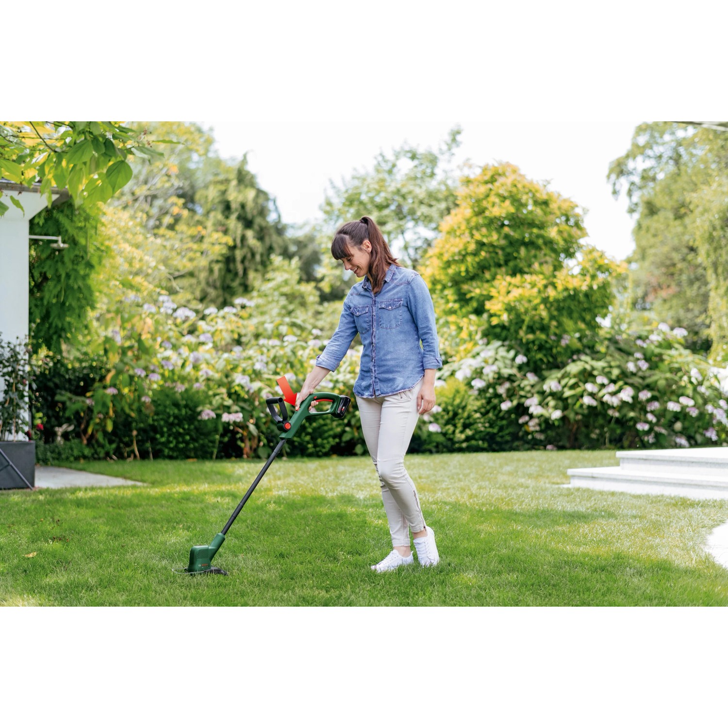 Frau trimmt Rasen mit Bosch Akku-Rasentrimmer EasyGrassCut 18V-230 im Garten.