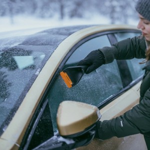 Frau kratzt mit Fiskars Auto-Eiskratzer Solid Orange-Schwarz die Autoscheibe frei.