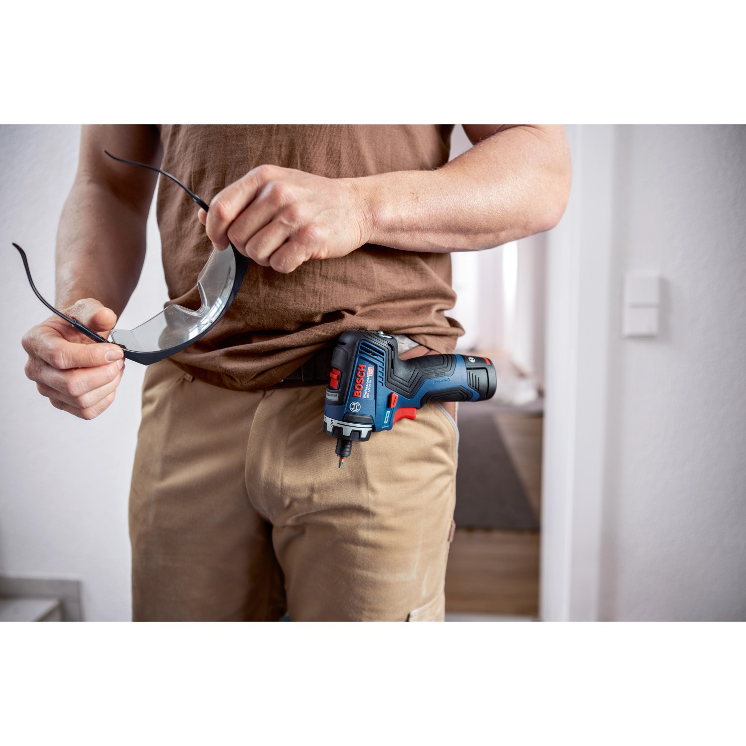 Bosch Professional Akku-Schlagbohrschrauber GSR 12V-35 am Gürtel mit Schutzbrille in der Hand.